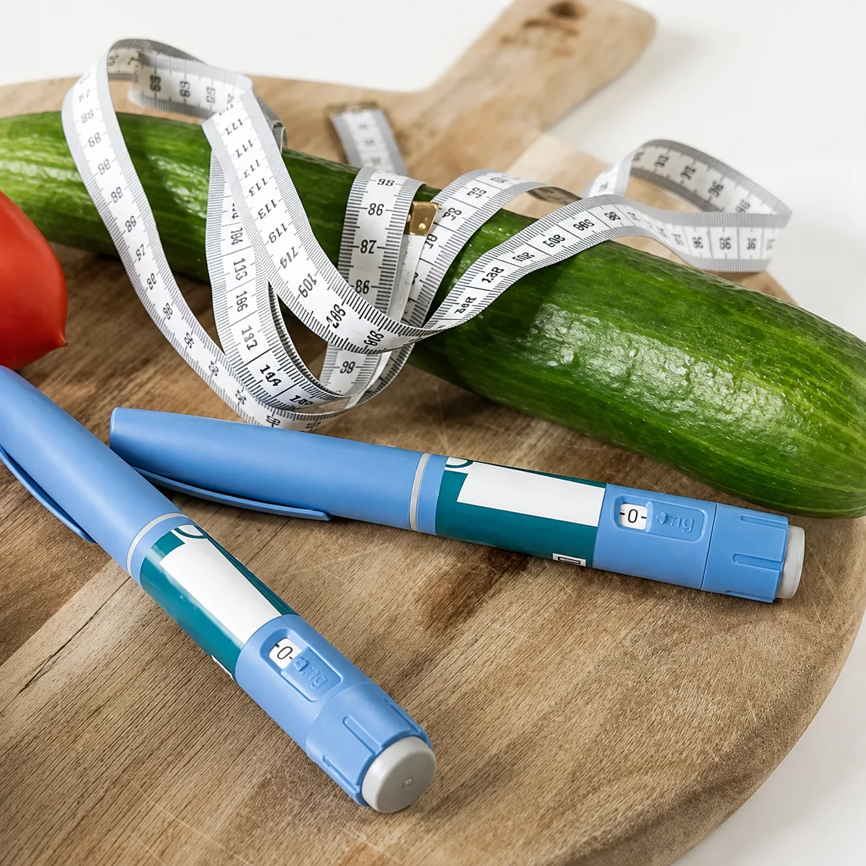 GLP-1 injection pens and a measuring tape on a cutting board with fresh vegetables