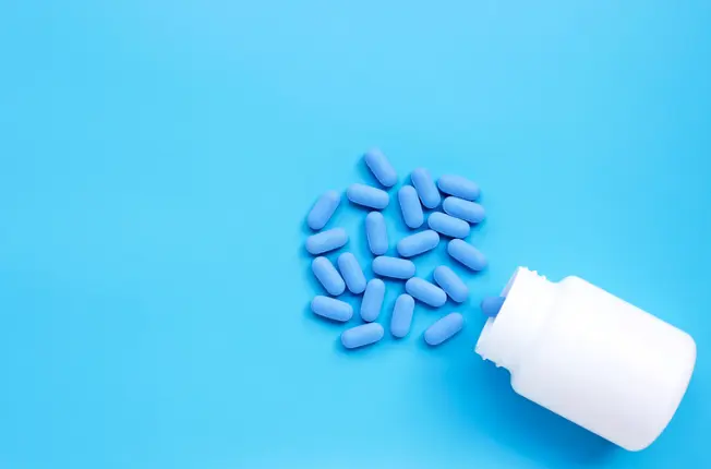 Blue PrEP tablets spilling from an open pill bottle
